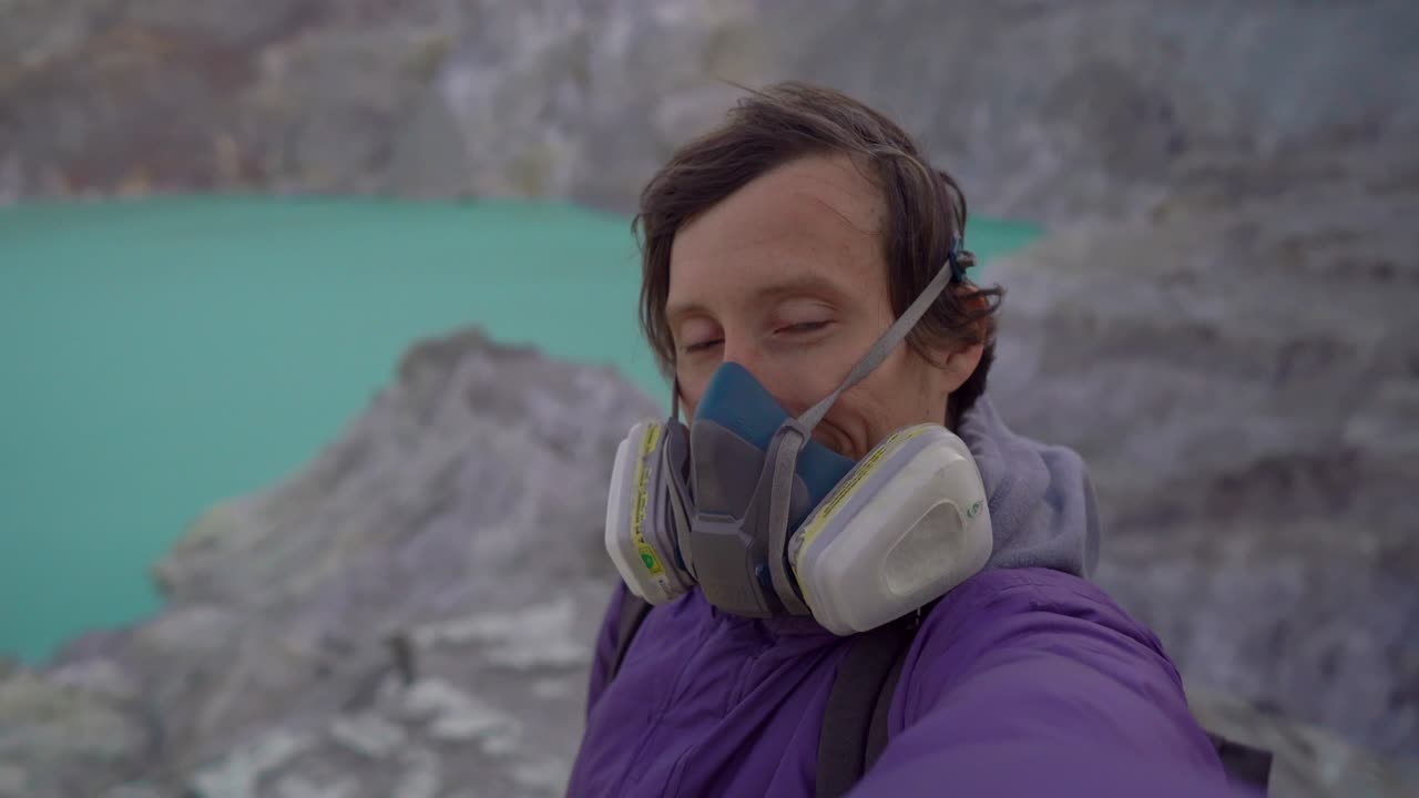 Young man traveler shoots a selfie video in the crater of the Ijen volcano or Kawah Ijen with a big acid lake in it. Java island, Indonesia