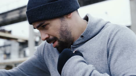 close-up view of caucasian man in grey hoodie hitting a punching bag outdoors an abandoned factory on a cloudy morning