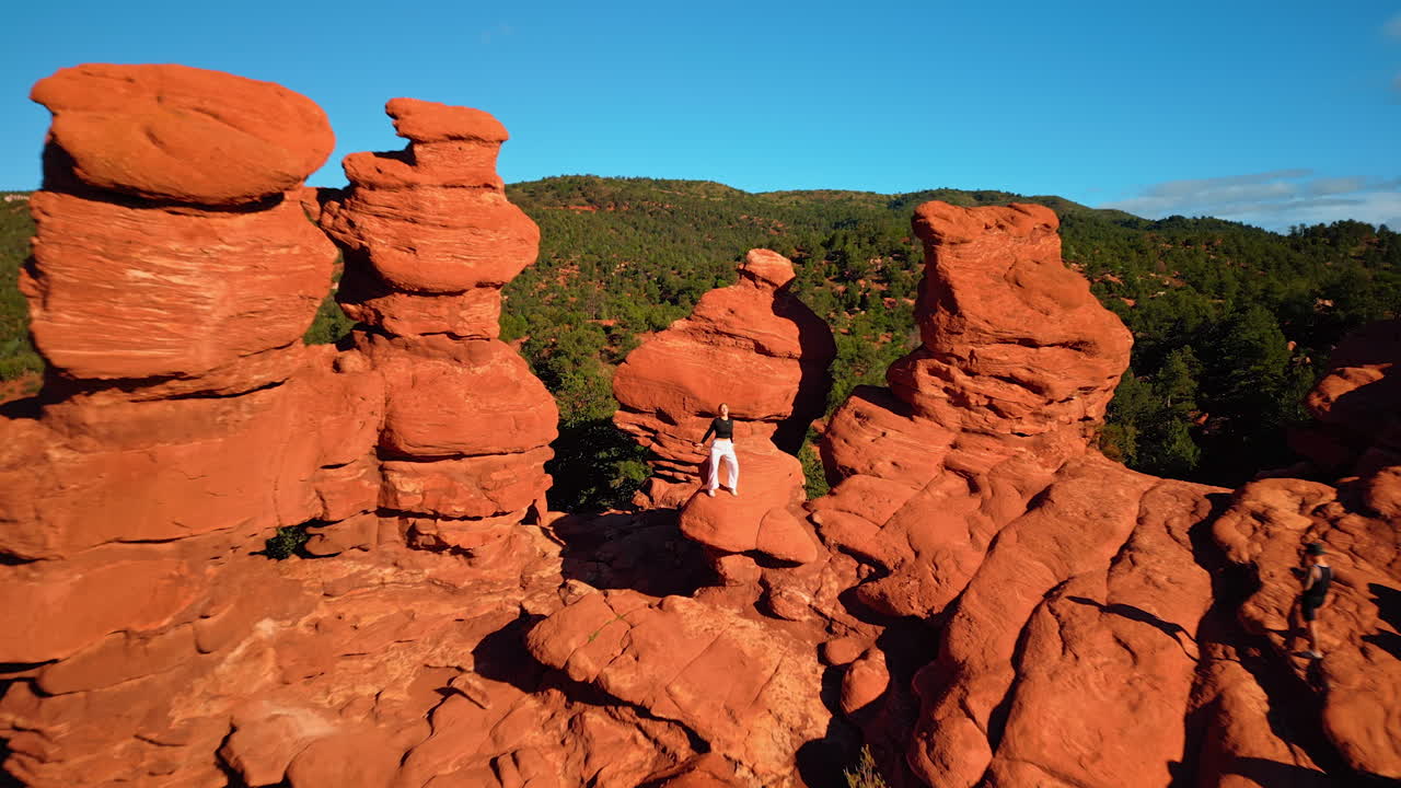 Flagstaff, USA, 24 August 2025: Distancing from the group of red rocks with a girl posing on them. Drone flight over the stunning territory of Garden of the Gods Park, Colorado Springs, Colorado, USA
