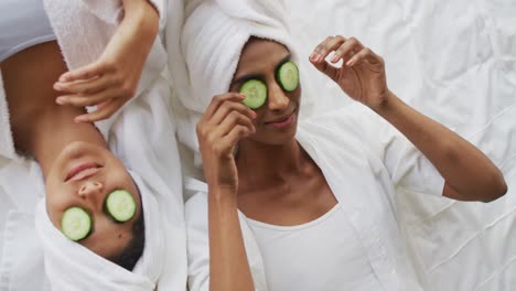 video of happy diverse female friends in robes having fun with cucumber slices