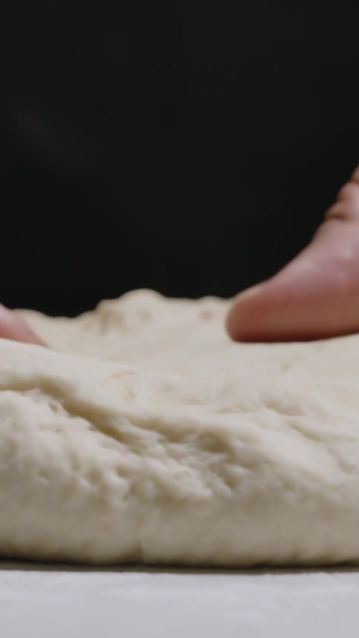 Vertikales Video: Handfläche schwebt, Hände drücken und dehnen Teig auf einem Vorbereitungsbrett, formen eine Schlaufe.