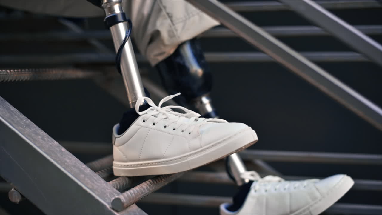 Slow motion view of a man with prosthetic legs and white sneakers sitting on a metal staircase
