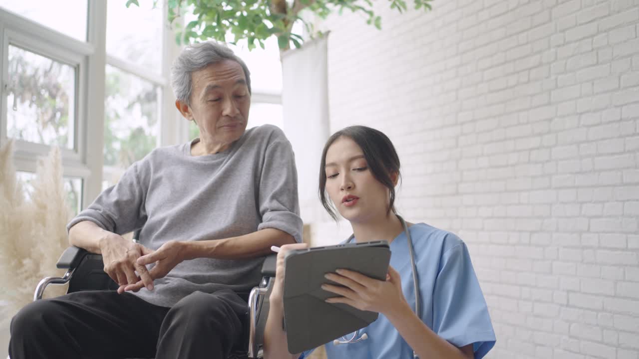 Young Asian nurse talking to a smiling senior female patient on a wheelchair and comforting her.
