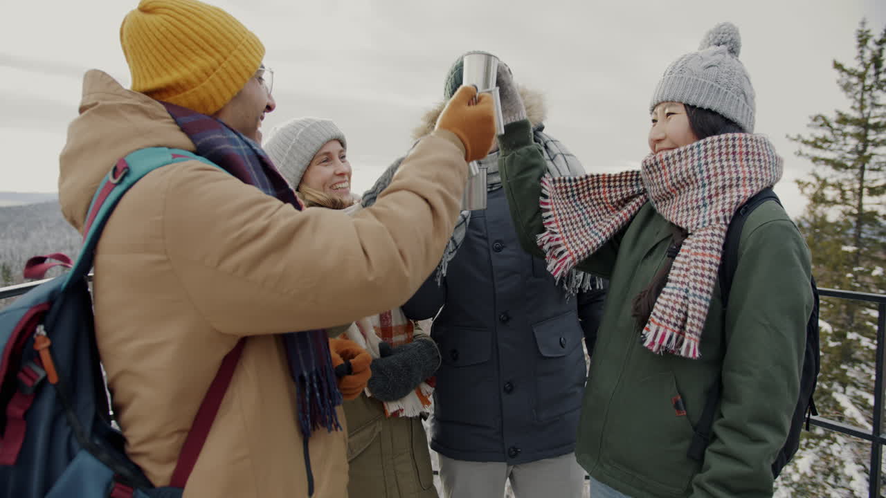 Friends toasting with hot drinks on a snowy mountaintop