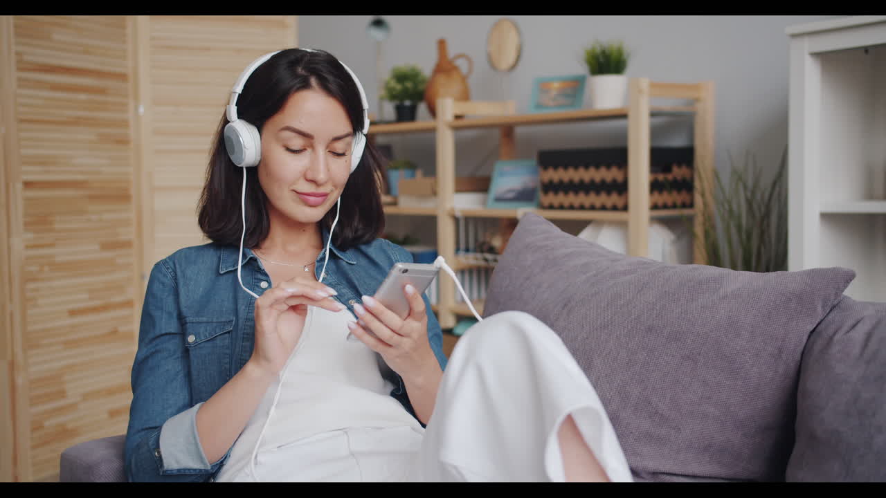 여성이 헤드폰과 전화로 소파에서 휴식을 취하고 있습니다.