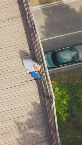newly wedded couple near railing on narrow wooden bridge over asphalt road on autumn day aerial view