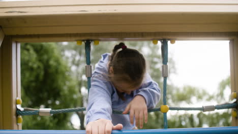 Kleines-Mädchen-Mit-Down-Syndrom,-Das-An-Einem-Windigen-Tag-Im-Netz-Eines-Kinderparks-Spielt