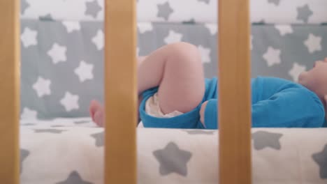 small baby kicks legs lying in new cot with stylish textile