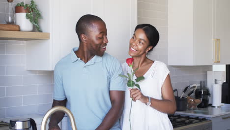 A-diverse-couple-shares-a-moment-in-the-kitchen,-surprising-with-gifts