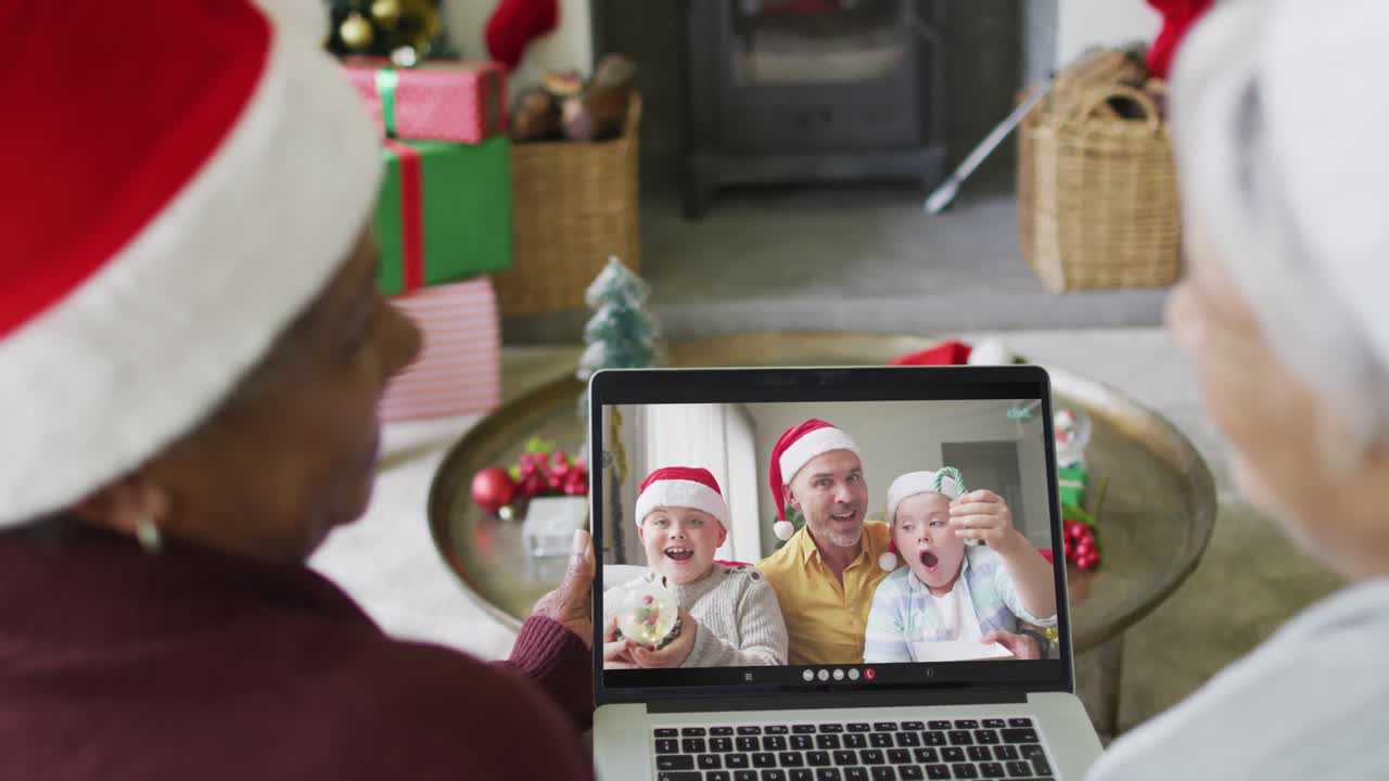 diversas amigas mayores que usan una computadora portátil para una videollamada de navidad con una familia sonriente en la pantalla