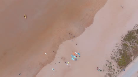 Rising-top-down-view-of-high-tide-mark,-colorful-surfboards-on-sandy-beach