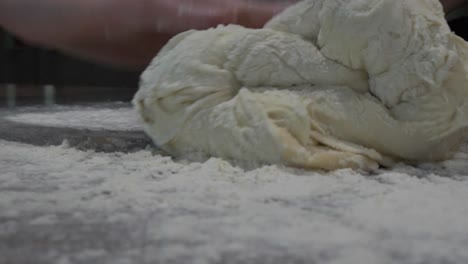 Pan-around-female-hands-preparing-and-kneeding-freshly-made-sourdough-bread-on-top-of-kitchen-bench-covered-in-flour