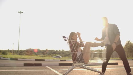 vista lateral de un joven y una mujer divirtiéndose al aire libre en carros de compras. jóvenes multiétnicos compitiendo en carros de compra. en la zona de estacionamiento con sus