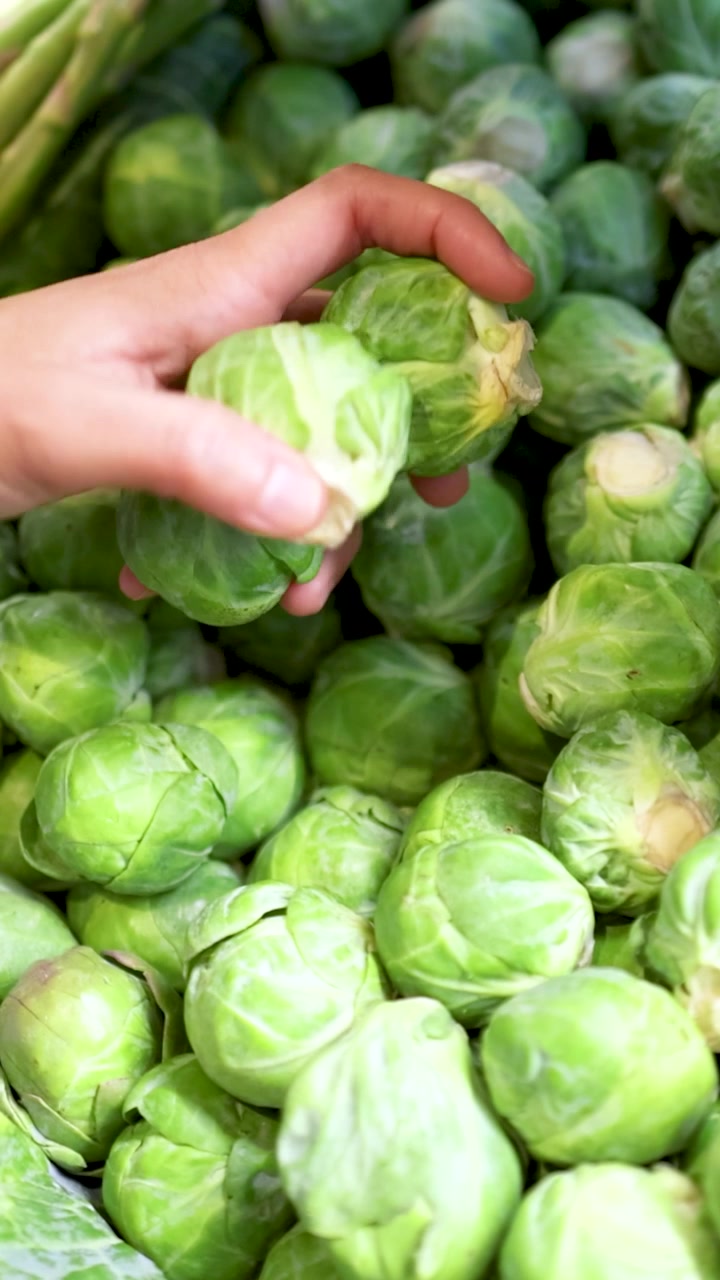 A hand picks fresh Brussels sprouts from a vibrant display under bright lighting in a Gold Coast supermarket