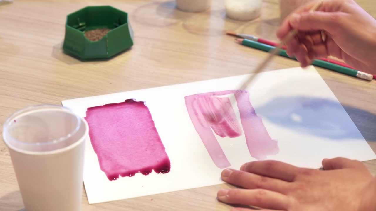 A woman in a studio painting on paper with red wine and brush, close view