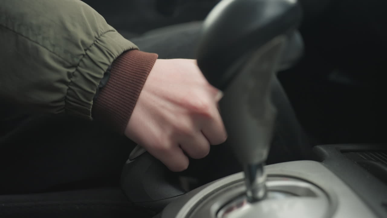 close up of driver hand pulling up parking brake lever and shifting gear into park on center console inside car cabin under soft daylight showcasing safe parking procedure with ergonomic comfort