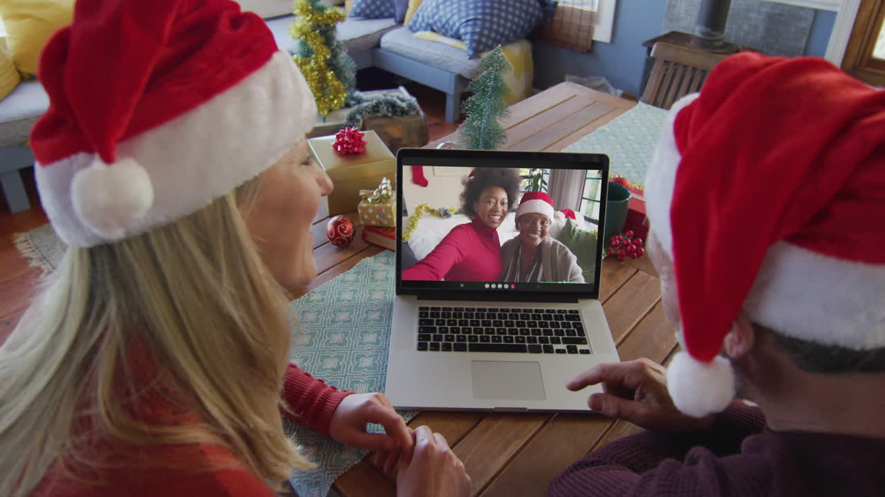 pareja caucásica sonriente con sombreros de santa usando una computadora portátil para una videollamada de navidad con la familia en la pantalla