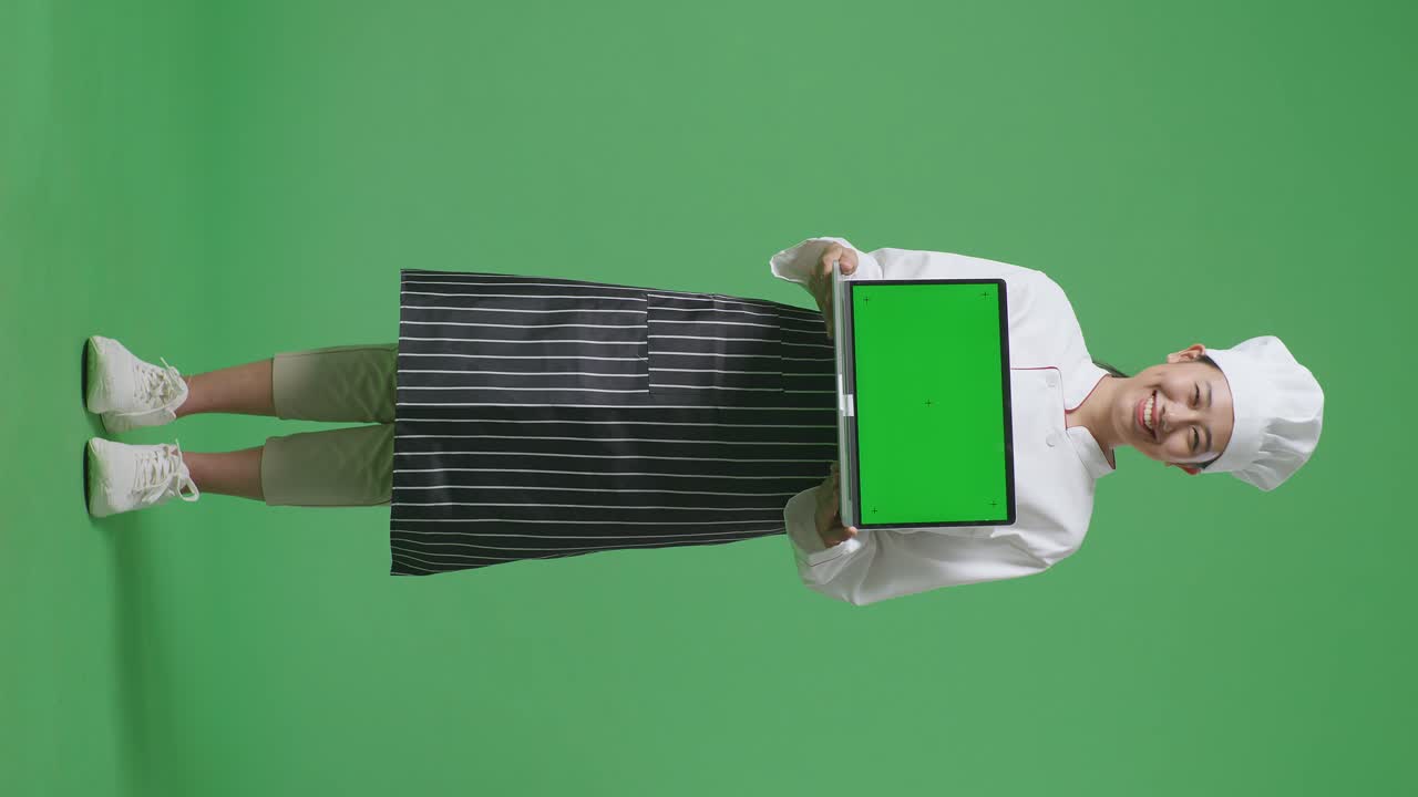 Full Body Of Asian Woman Chef Smiling And Showing Green Screen Laptop To The Camera While Standing In The Green Screen Background Studio
