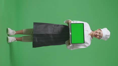 full body of asian woman chef smiling and showing green screen laptop to the camera while standing in the green screen background studio