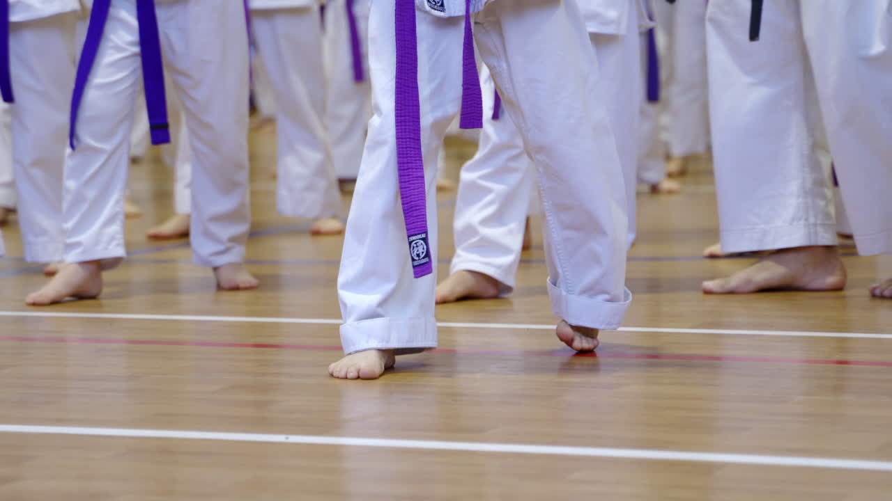 Barefoot practicing kicks at karate training. The legs of young athletes doing exercise standing on wooden floor.