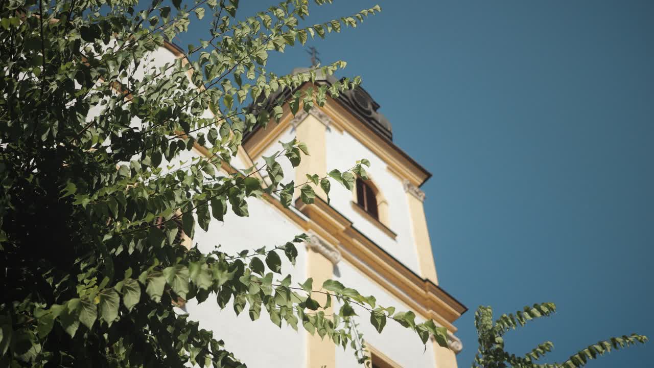 Historic church tower with trees and clear sky, calm sunny afternoon
