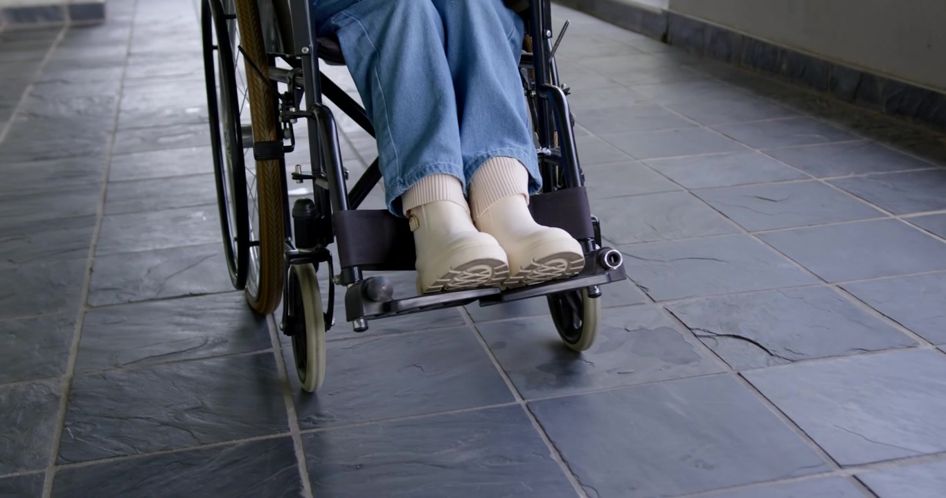 Donna seduta su una sedia a rotelle manuale che aziona i corrimano, percorrendo un corridoio piastrellato per spostarsi