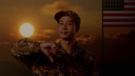 close up of asian man soldier showing thumbs down gesture to camera while standing with flag of the united states, sunset time