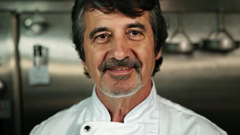 a smiling chef in a white chef coat stands in a kitchen