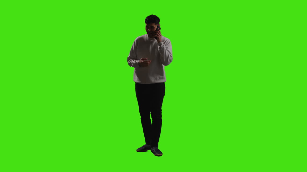 Giovane uomo che effettua una chiamata sul cellulare in piedi davanti a uno schermo verde con illuminazione a bassa chiave