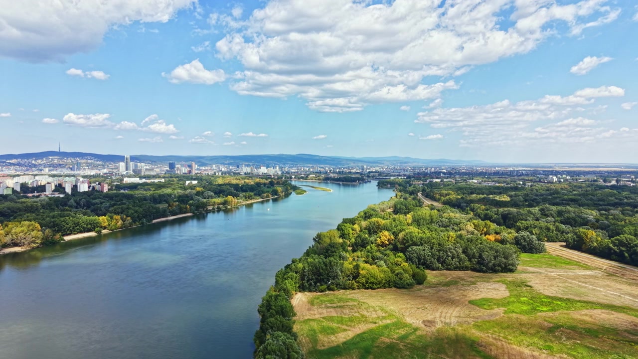 Vista panoramica di un fiume che si snoda attraverso alberi verdi e campi vicino a una città sotto un cielo blu con nuvole