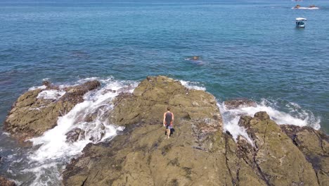 toma aérea de seguimiento de un joven navegando por la ruta más segura hasta el borde de las rocas