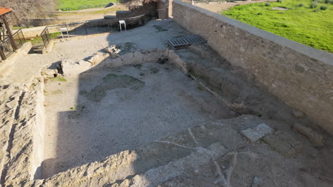 An-ancient-excavation-site-with-stone-foundations-and-walls,-featuring-a-small-structure-with-a-tiled-roof-in-Pafos