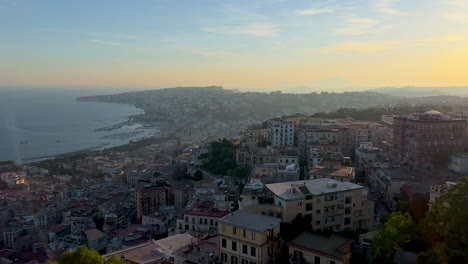 Una-Vista-Panorámica-De-Una-Ciudad-Costera-Durante-El-Amanecer-O-El-Anochecer,-Con-Edificios-Densamente-Poblados-En-Una-Ladera-Con-Vistas-A-Una-Tranquila-Bahía-De-Nápoles,-Italia