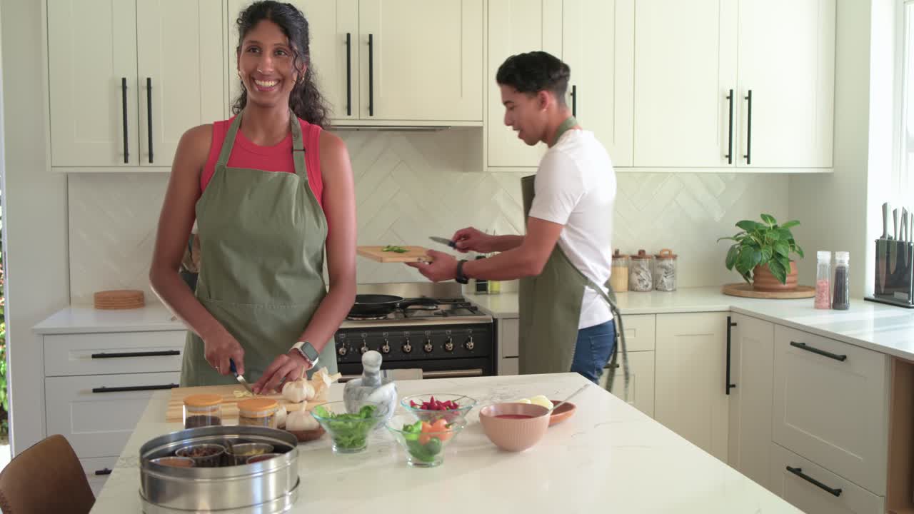 Amigos de avental colocando tábuas, então picando na ilha da cozinha, movendo-se para o fogão, preparando refeição.