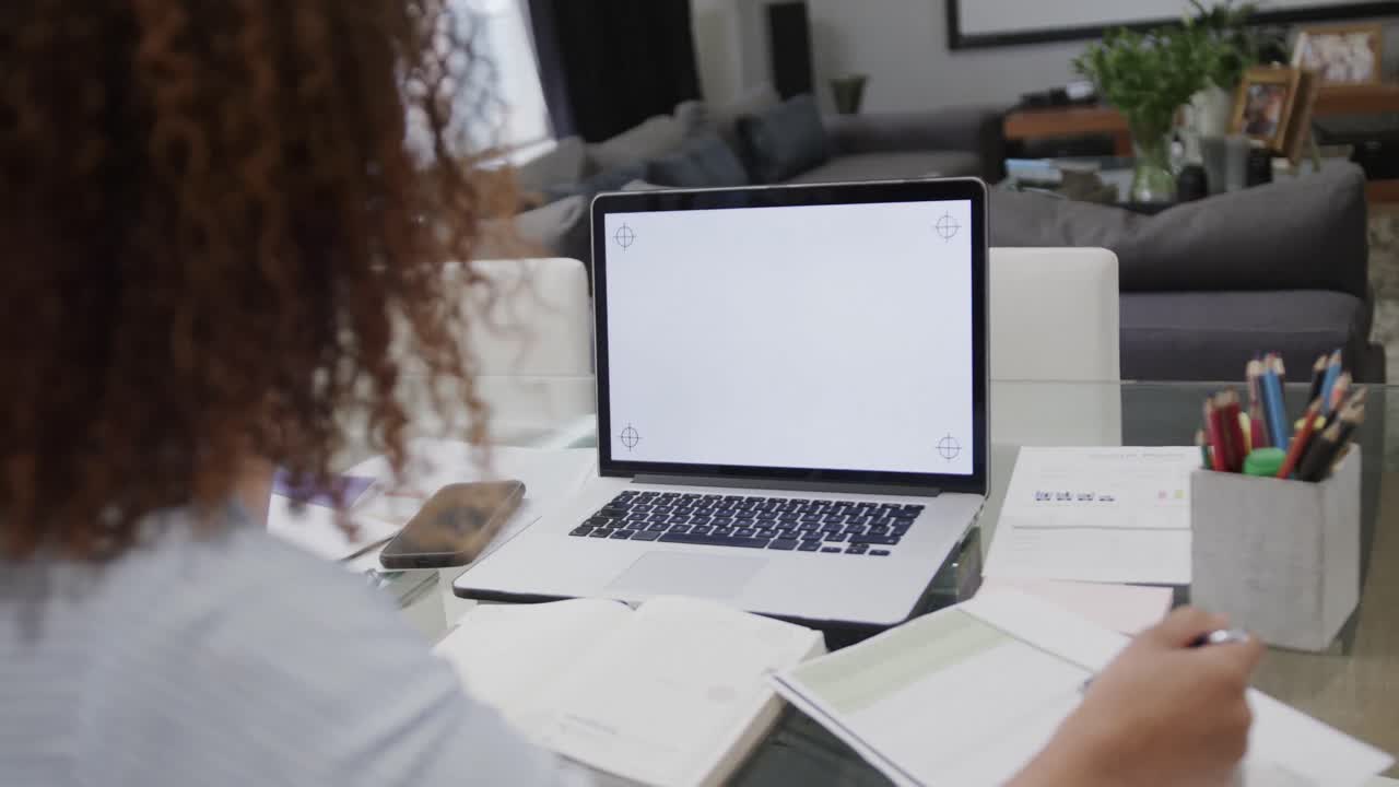 mujer biracial que trabaja en casa haciendo una llamada de video en una computadora portátil con espacio de copia en la pantalla, en cámara lenta