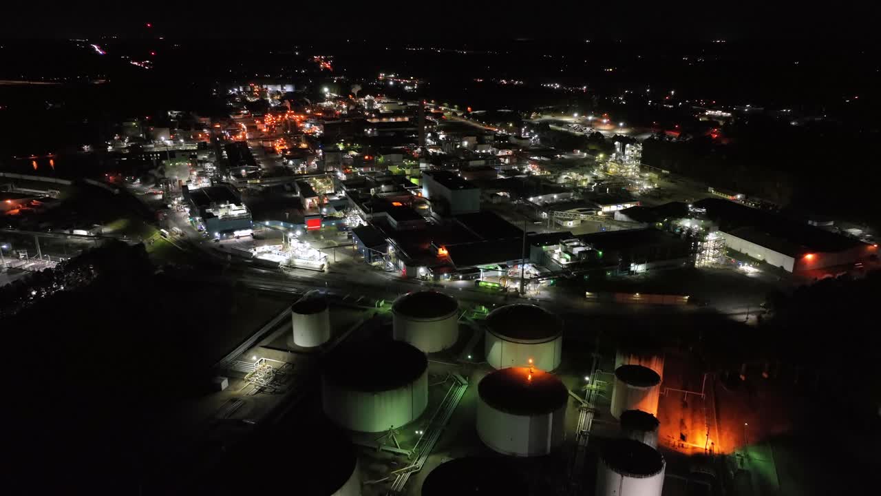 Aerial night view of large industrial complex with illuminated storage tanks, factories, pipelines and city lights glowing across surrounding area. DuPont power plant in Richmond, Va