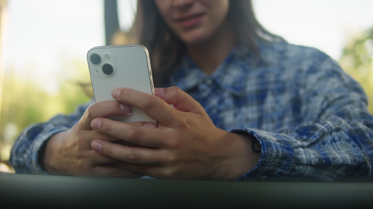 Woman is chatting with friends with phone in the park. Student girl sitting outside drinking coffee and communicating wit smartphone.