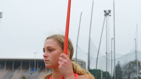vista frontal de una atleta caucásica de pie con un palo de jabalín en un lugar deportivo 4k