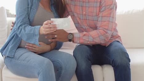 expecting couple sitting on couch, holding ultrasound image and smiling