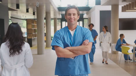 retrato de un médico de sexo masculino con trajes de exfoliación doblando los brazos y de pie en un hospital ocupado