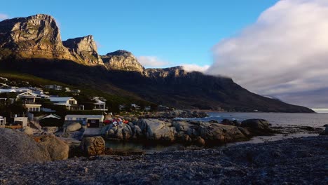 fast paced clouds - ocean waves moving in on resort at the base of south african apostles mountain range.