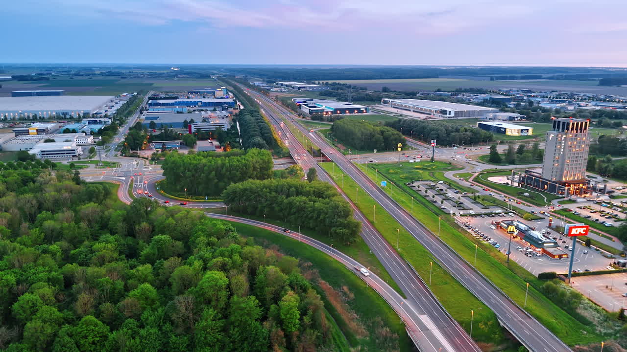 Lively traffic on the highways at the suburbs on the city. Malls and storehouses surrounded by forests and fields. Aerial perspective.