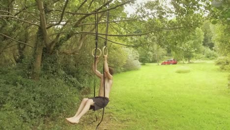 athletic young man doing ring pullups in garden