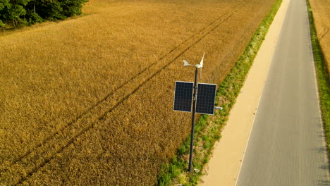 wind generator and solar panel system on lighting pole near yellow wheat field and asphalt road in countryside