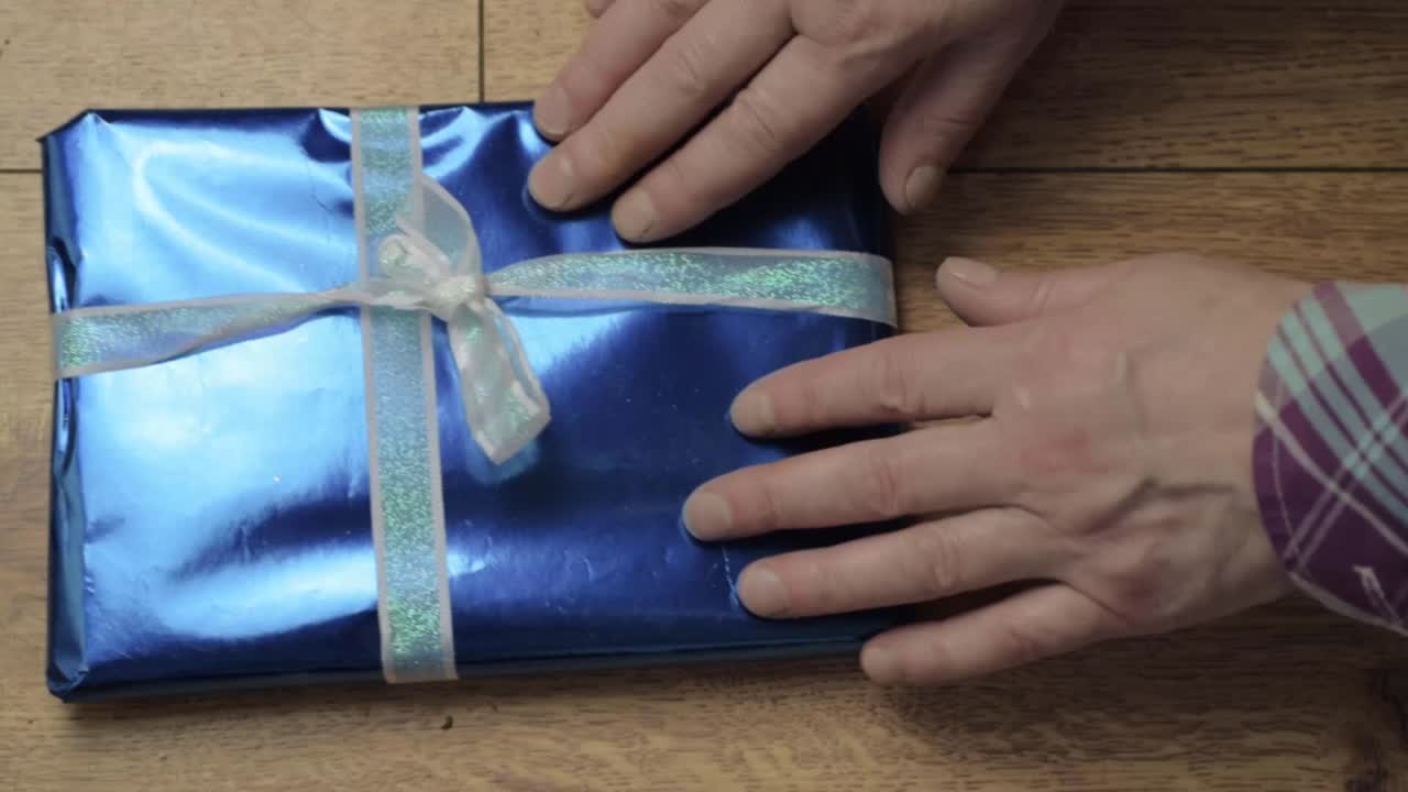Hand unwrapping Christmas gift with ribbon and blue paper flatlay medium shot