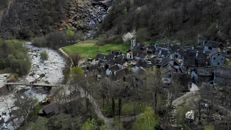 aerial flyover over foroglio in ticino, switzerland with a pan up motion up from the rooftops of the old stone houses in the village up to the waterfall at dusk