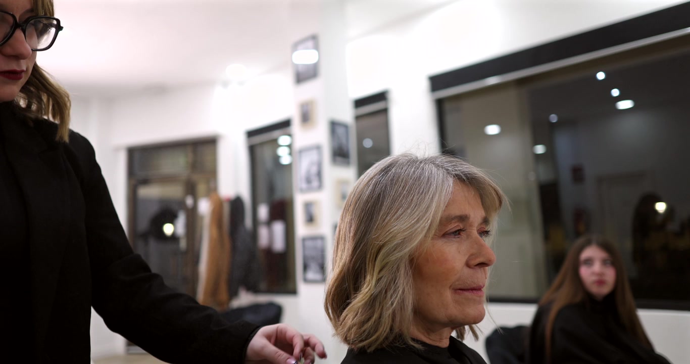 Parrucchiera professionista che acconcia i capelli di una donna matura in salone