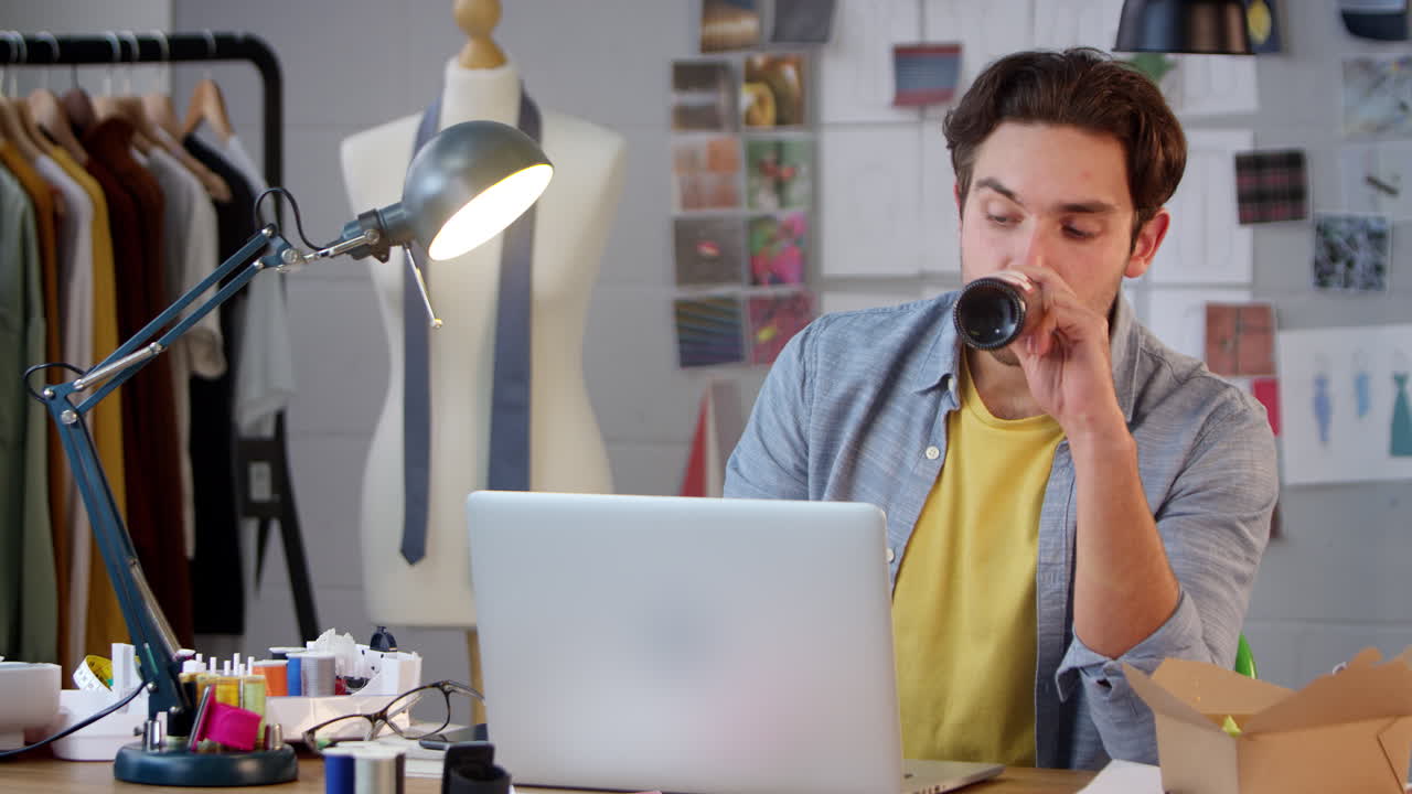 Stanco titolare di un'attività di moda con una bottiglia di birra che lavora fino a tardi al laptop in studio