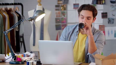 hombre cansado dueño de un negocio de moda con una botella de cerveza trabajando hasta tarde en la computadora portátil en el estudio