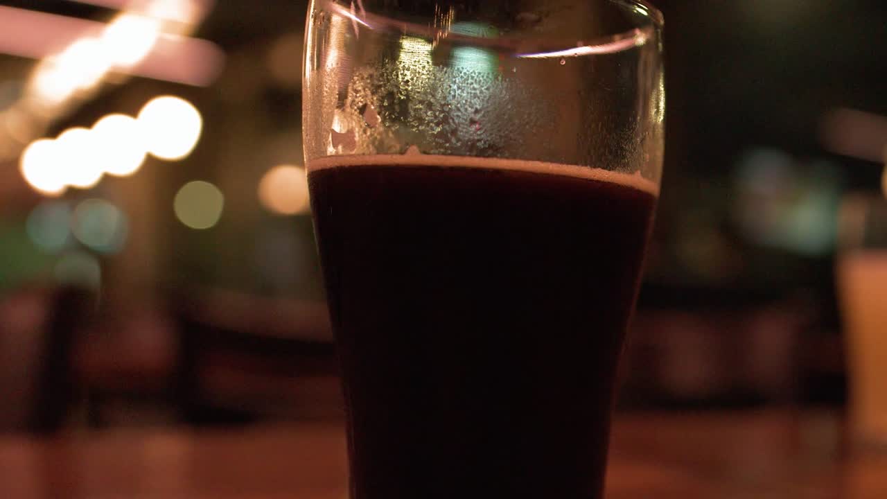 Scatto ravvicinato e centrato di una birra artigianale scura con luci bokeh sullo sfondo.